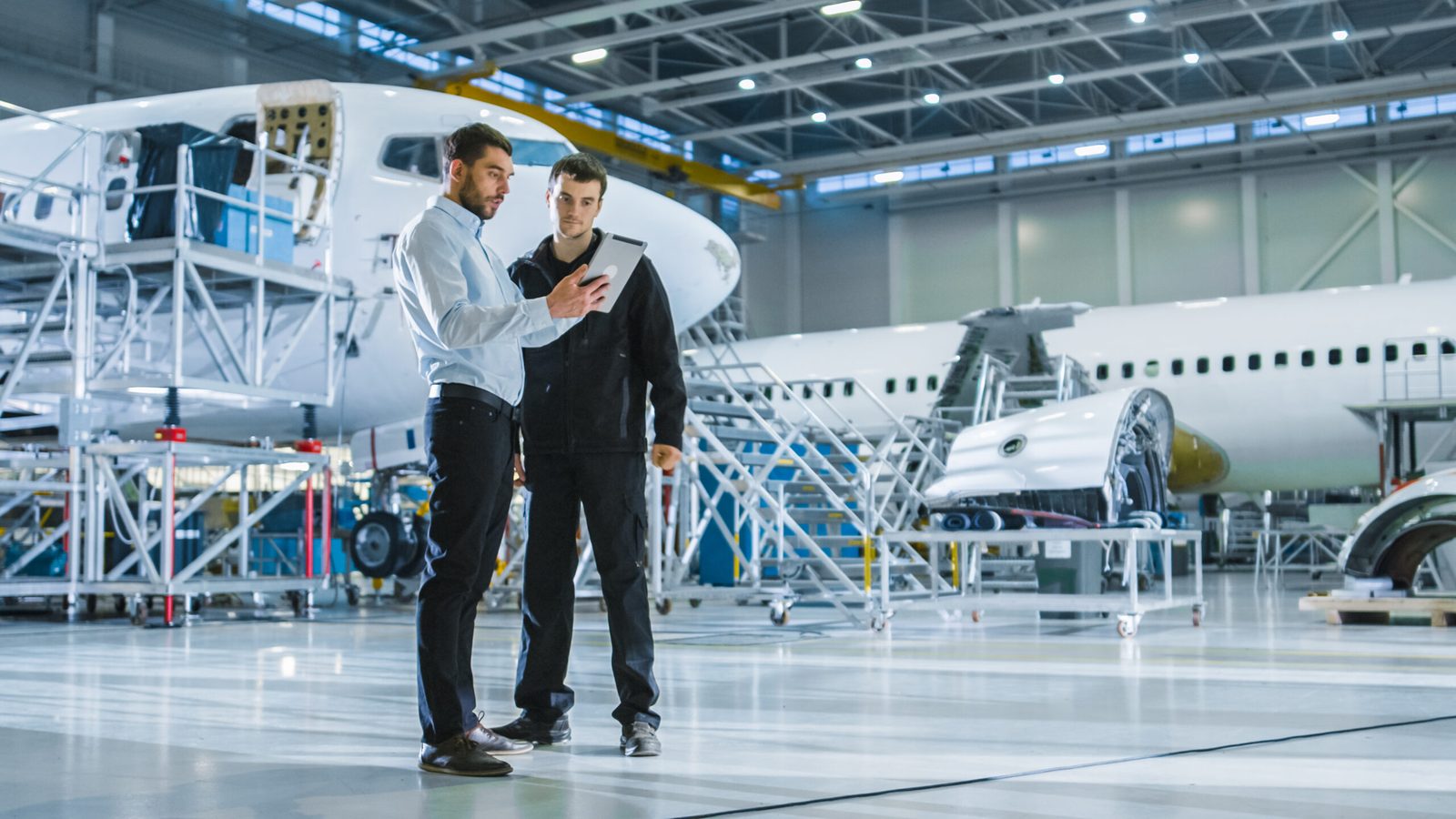 Engineers reviewing work on a tablet inside an aircraft hangar